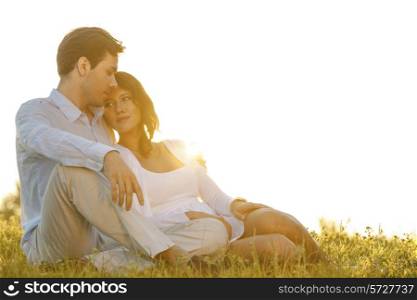 Loving young couple sitting on grass against clear sky
