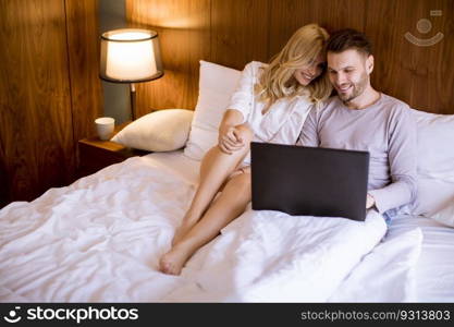 Loving young couple surfing internet on laptop in the bed at home