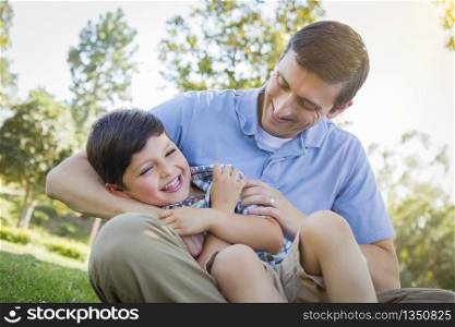 Loving Young Father Tickling Son in the Park.