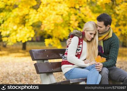 Loving young man hugging shy woman on park bench during autumn
