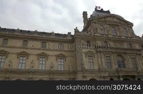 Low agnle steadicam shot of moving along the Louvre, world largest museum in Paris. French flag waving on the top