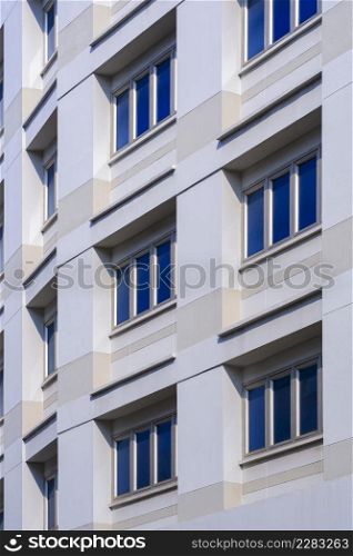 Low angle and perspective side view of multiple closed blue glass windows on office building wall in vertical frame