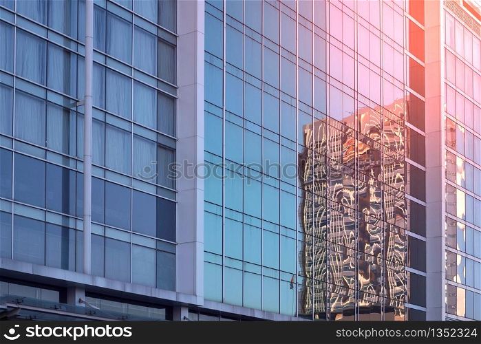 Low angle and side view of blue glass wall with reflection pattern of skyscraper and flare light on surface, architecture and buildings exterior design concept