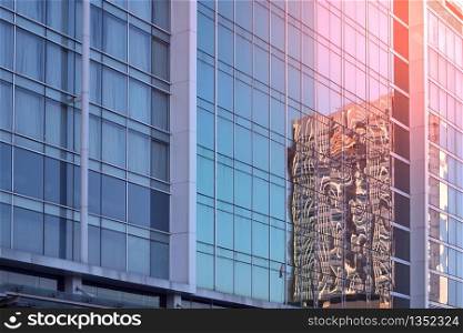Low angle and side view of blue glass wall with reflection pattern of skyscraper and flare light on surface, architecture and buildings exterior design concept