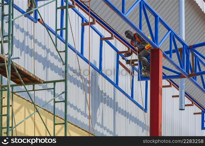 Low angle and side view of construction workers are lifting metal framework for install on top of warehouse structure in construction site near the industrial building