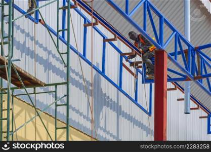 Low angle and side view of construction workers are lifting metal framework for install on top of warehouse structure in construction site near the industrial building