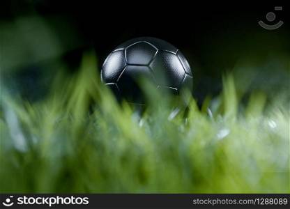 Low-angle close-up of a black soccer ball on the green grass of the football ground against dark background for copy space