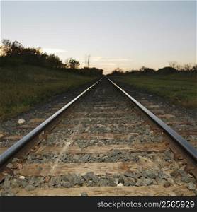 Low angle diminishing view of railroad tracks in rural setting at dusk.