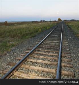 Low angle diminishing view of railroad tracks in rural setting at dusk.