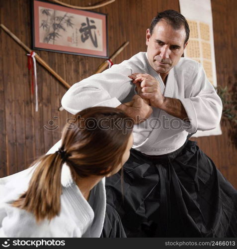 low angle male martial arts instructor training with female trainee practice hall