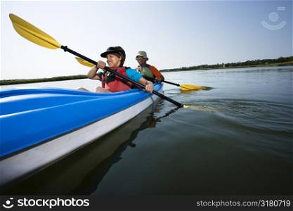 Low angle of African American middle-aged man and woman paddling kayak.