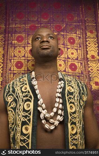 Low angle portrait of African-American mid-adult man wearing embroidered African vest and beads.