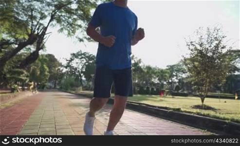 Low angle shot: a middle aged man on jogging along the public park runway, body wellness tired exhausted, men heath, elderly retired life, afternoon cardio workout, life insurance, elderly health care