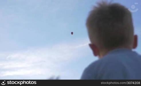 Low-angle shot of a boy waving hand to sky lantern flying high in the air.