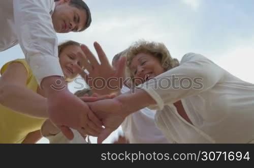 Low-angle shot of a large family putting hands together and lifting them up.