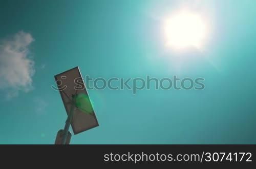 Low angle shot of a street light equipped with solar batter on the background of blue sky and sun. Alternative energy sources