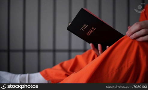 Low angle shot of an inmate reading a bible in prison