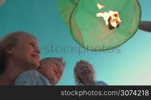 Low angle shot of mother, son and grandmother looking at the fire inside green sky lantern which family is going to launch