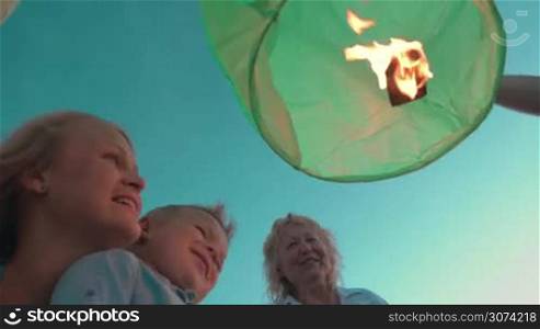 Low angle shot of mother, son and grandmother looking at the fire inside green sky lantern which family is going to launch