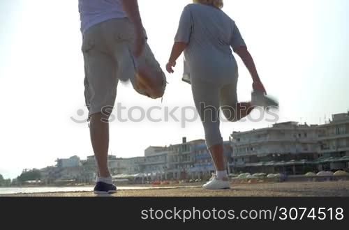 Low angle shot of senior couple warming up on the pier before physical training. They stretching legs against bright sunlight and starting the jog
