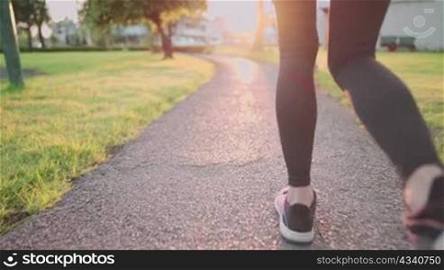 Low angle shot rear view of young sporty woman run inside the park on the running path way, beautiful orange sunset horizon light, cardio exercise, beginning of new sport resolution positive energy