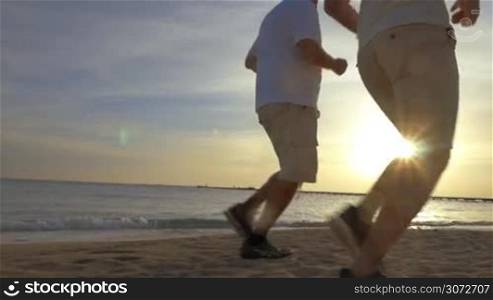 Low-angle steadicam shot of two men jogging on the beach, their legs are in shot.