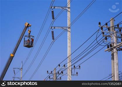 Low angle view and selective focus at crane truck lifting 2 electricians in metal man basket to working on electric power poles against blue clear sky background
