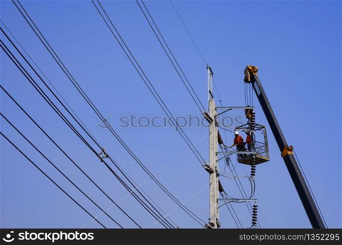 Low angle view and selective focus at crane truck lifting 2 electricians in metal man basket to working on electric power pole against blue clear sky background