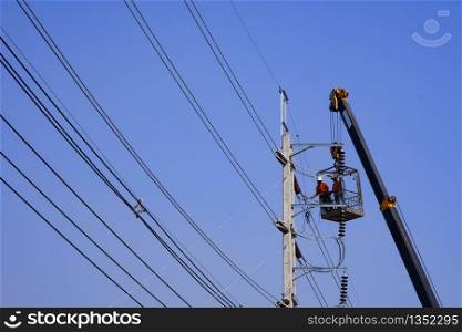 Low angle view and selective focus at crane truck lifting 2 electricians in metal man basket to working on electric power pole against blue clear sky background