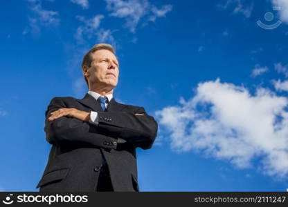 low angle view businessman standing with folded arms against sky