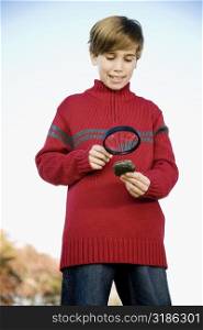 Low angle view of a boy looking at a rock through magnifying glass
