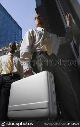 Low angle view of a businessman holding a briefcase and another businessman standing behind him