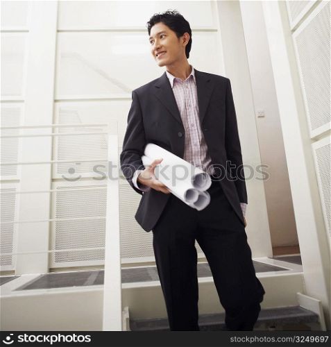 Low angle view of a businessman holding blueprints and smiling
