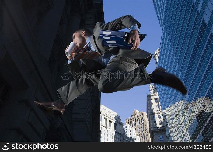 Low angle view of a businessman jumping in mid-air and drinking