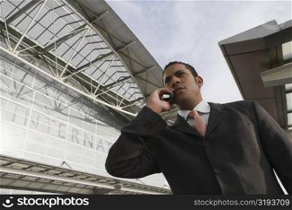 Low angle view of a businessman talking on a mobile phone outside an airport