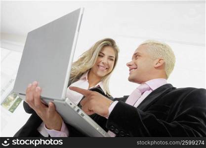 Low angle view of a businesswoman and a businessman using a laptop and smiling