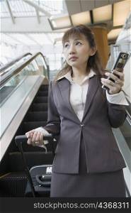 Low angle view of a businesswoman holding a mobile phone and a suitcase