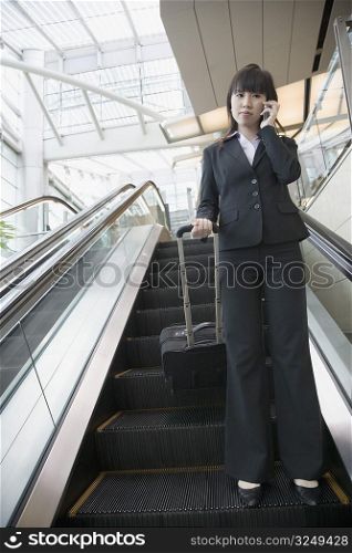 Low angle view of a businesswoman standing on an escalator and talking on a mobile phone