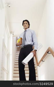 Low angle view of a male architect holding rolled up blueprints and a hardhat