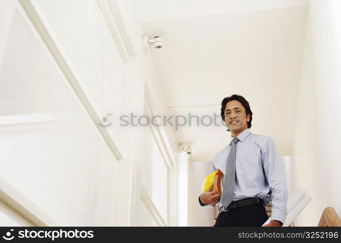 Low angle view of a male architect holding rolled up blueprints and a hardhat