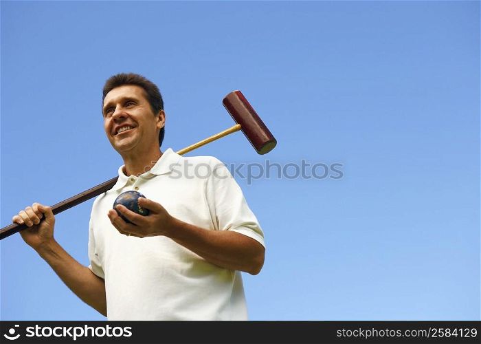 Low angle view of a mature man holding a croquet mallet and a ball