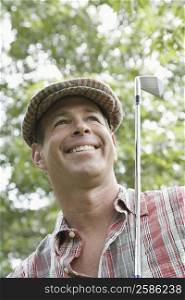 Low angle view of a mature man holding a golf club and smiling