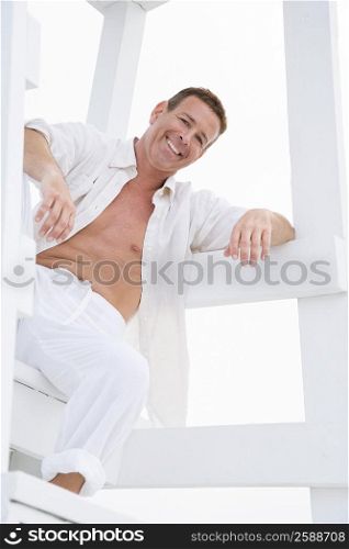 Low angle view of a mature man sitting on a lifeguard hut and smiling