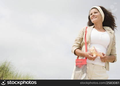 Low angle view of a mature woman holding a conch shell and smiling