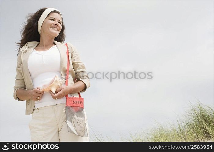 Low angle view of a mature woman holding a conch shell and smiling