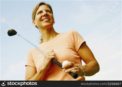 Low angle view of a mature woman holding a golf club and a golf ball