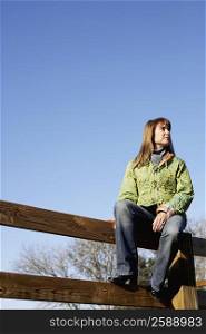 Low angle view of a mature woman sitting on a fence