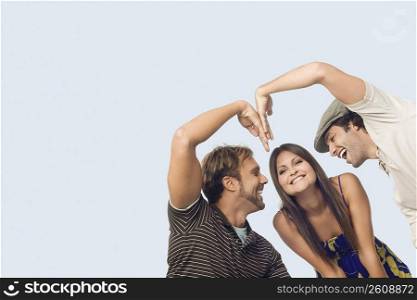 Low angle view of a mid adult man and a young man making a heart shape in front of a young woman