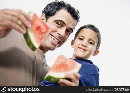 Low angle view of a mid adult man carrying his son and holding watermelon slices
