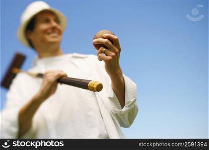 Low angle view of a mid adult man holding a croquet mallet and a ball
